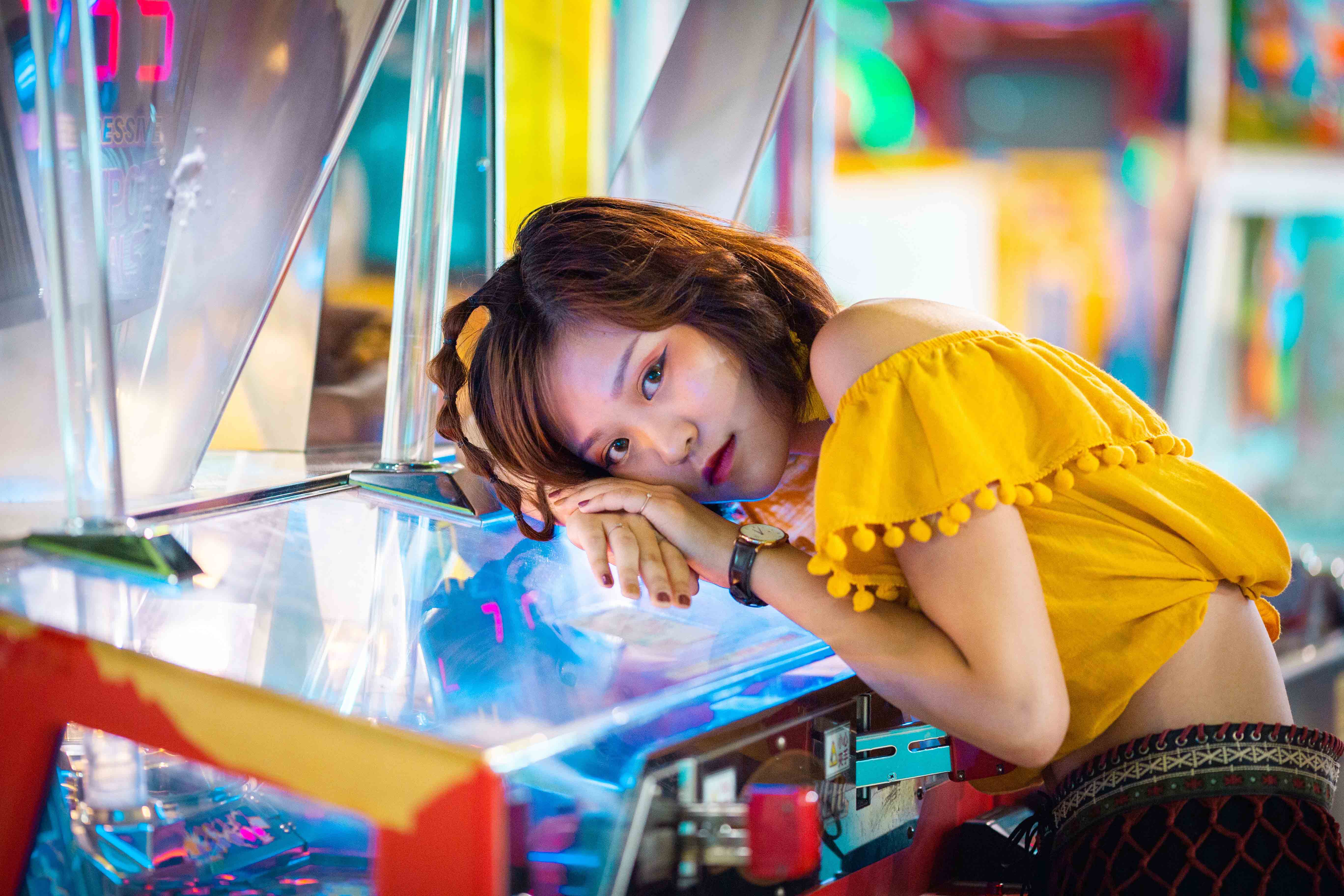  A photo of a woman in a yellow top, leaning on an arcade machine