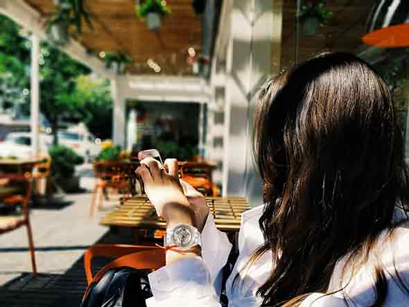 A photo of a woman sitting outside a cafe, holding a smartphone