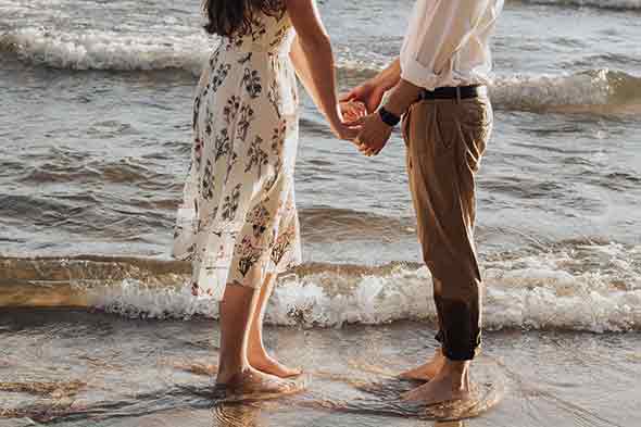 A photo of a man and woman holding hands at the beach