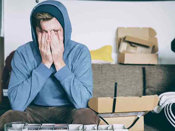 man in blue hoodie covering his face sitting on sofa