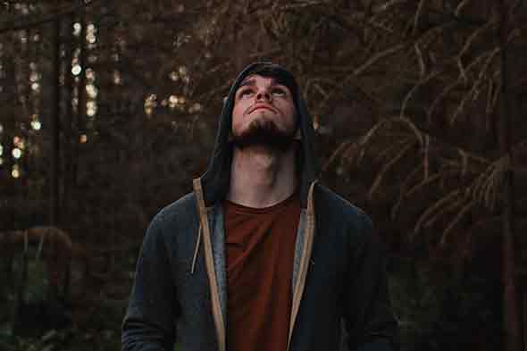 A man wearing brown shirt and gray hoodie standing on the woods.