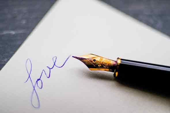 A photo of a fountain pen on top of paper with the word love written on it