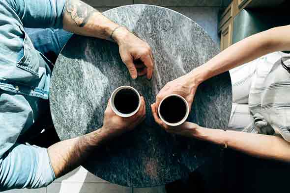 A photo of a couple sitting across from each other, each with a cup of coffee in hand