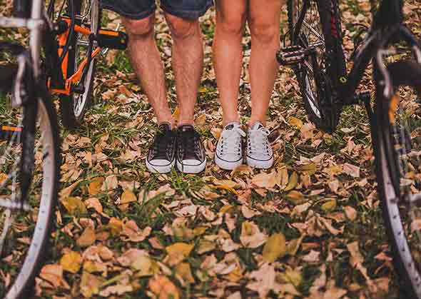 A photo of a couple’s legs with bikes beside each of them,standing on grass and leaves