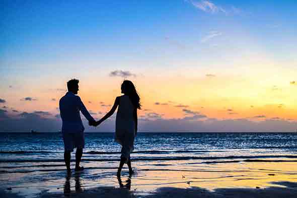 Man and woman holding hands by the seashore.