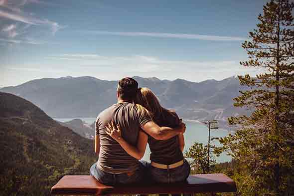 man and woman sitting on a bench overlooking mountains
